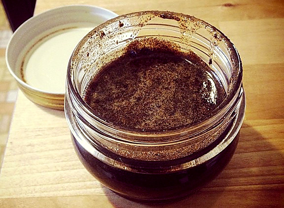 An open jar of dark homemade vanilla bean paste, flecked with vanilla seeds